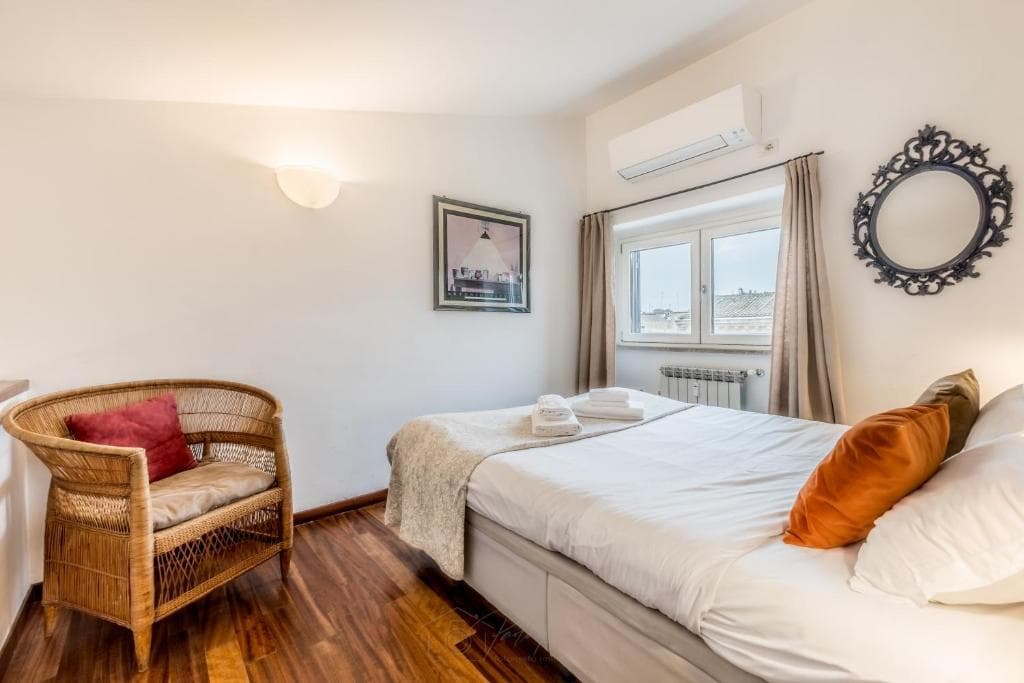 Mezzanine bedroom with wicker chair and a window onto the rooftops